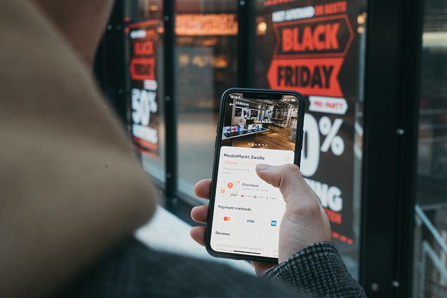 male holding an iPhone in front of a Black Friday sales sign